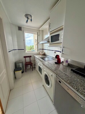 A compact kitchen with a washing machine, a microwave, and a sink. - Apartment in Mogro first line of beach (Miengo)