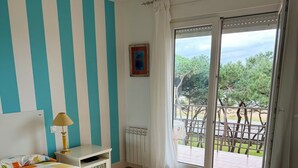 A bedroom with a bed, a nightstand, a lamp, a radiator, and a sliding glass door leading to an outdoor area.