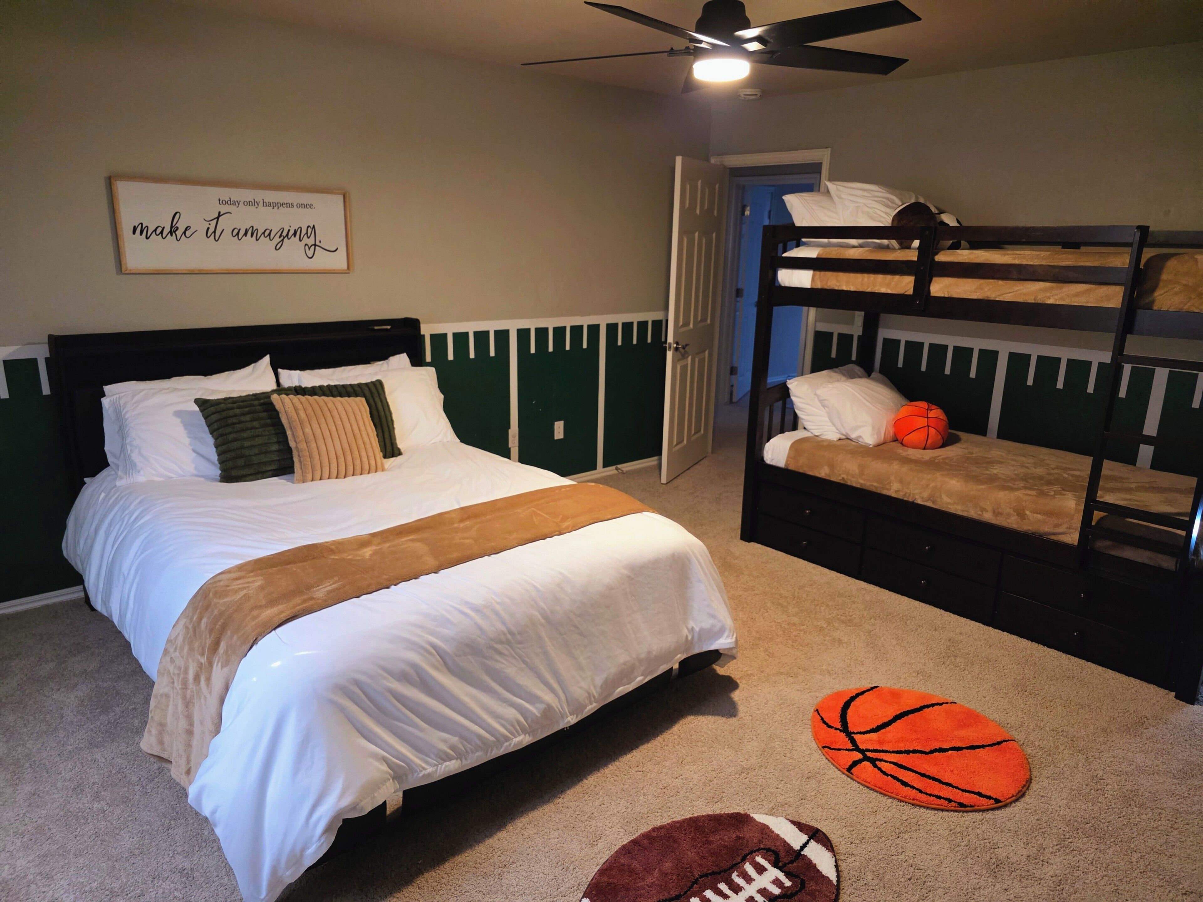 A bedroom with a bed, a bunk bed, a ceiling fan, a motivational quote on the wall, and two sports-themed rugs.