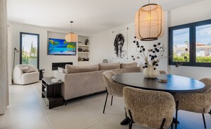 A modern living room with a sofa, a dining table with chairs, a TV, and artwork on the walls. - Elegant Villa With sea Views & Pool Marbella (Marbella)