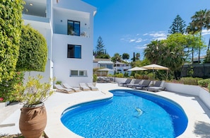 A modern pool area with a curved pool, lounge chairs, and a potted plant. - Elegant Villa With sea Views & Pool Marbella (Marbella)