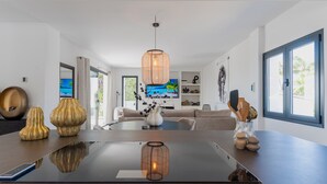 Una sala de estar moderna con una gran mesa de comedor, un sofá y un televisor que muestra una escena de playa.