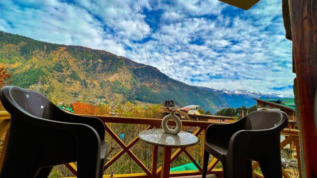 Un balcone con due sedie e un tavolino, affacciato su un paesaggio montuoso con cielo sereno.
