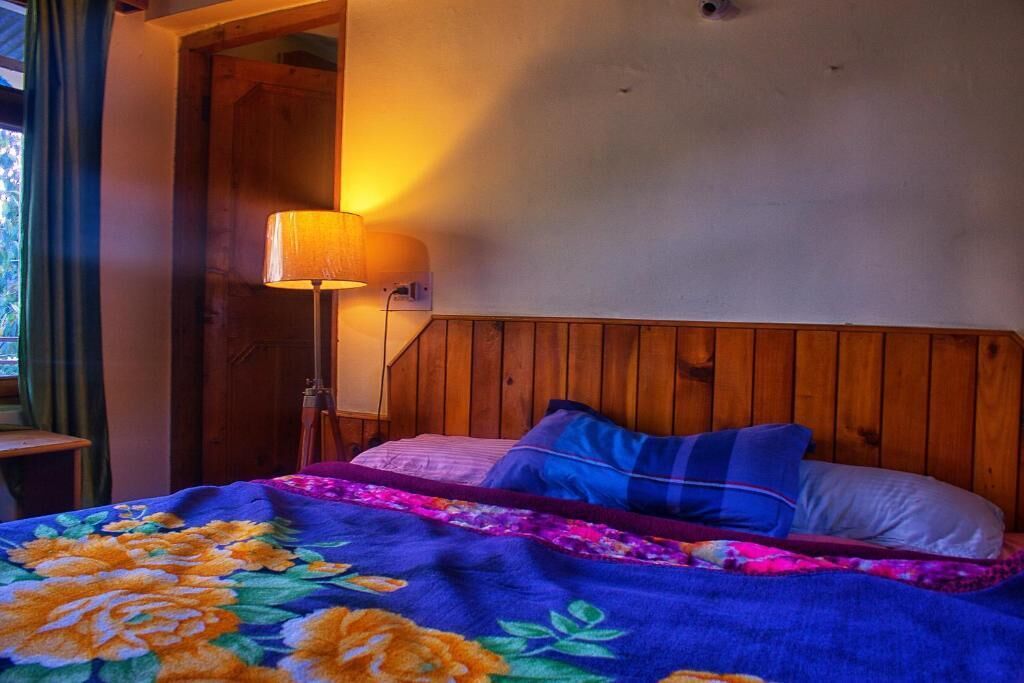 A bedroom with a wooden headboard, a bed with floral bedding, and a bedside lamp.