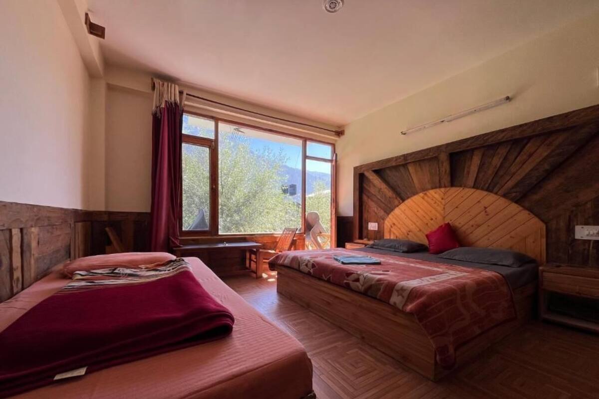 A room with two beds, wooden walls, a large window, and a view of greenery.