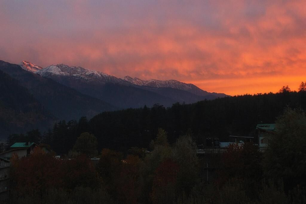 A mountainous landscape with a sunset, featuring snow-capped peaks and a forested valley.