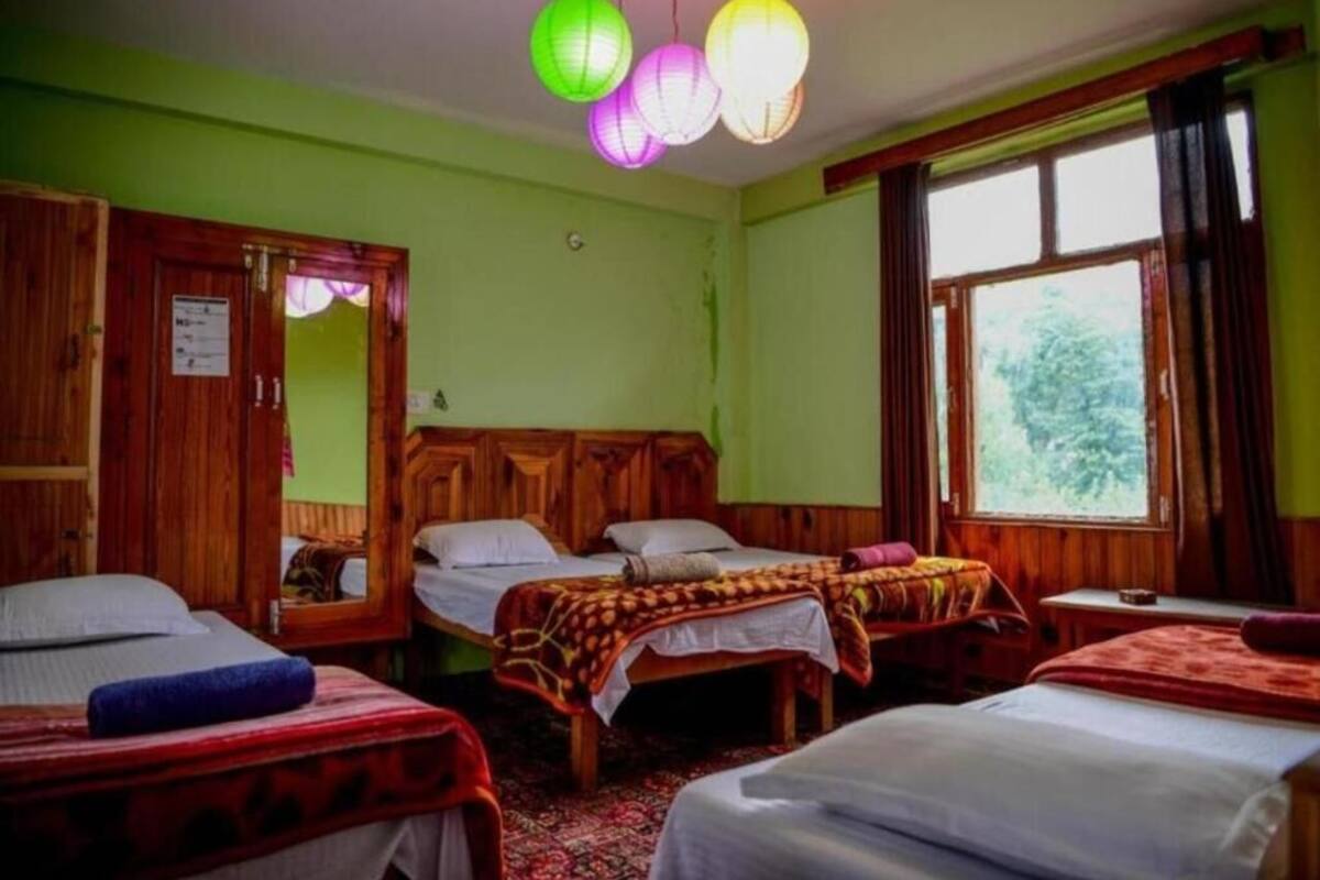 A room with three wooden beds, a wooden wardrobe, and a window with curtains.