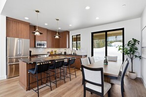 A modern kitchen with wooden cabinets, stainless steel appliances, a central island with bar stools, and a dining area with a table and chairs. - -Luxury Ski-In/Ski-Out Brundage Home Near McCall- (McCall)