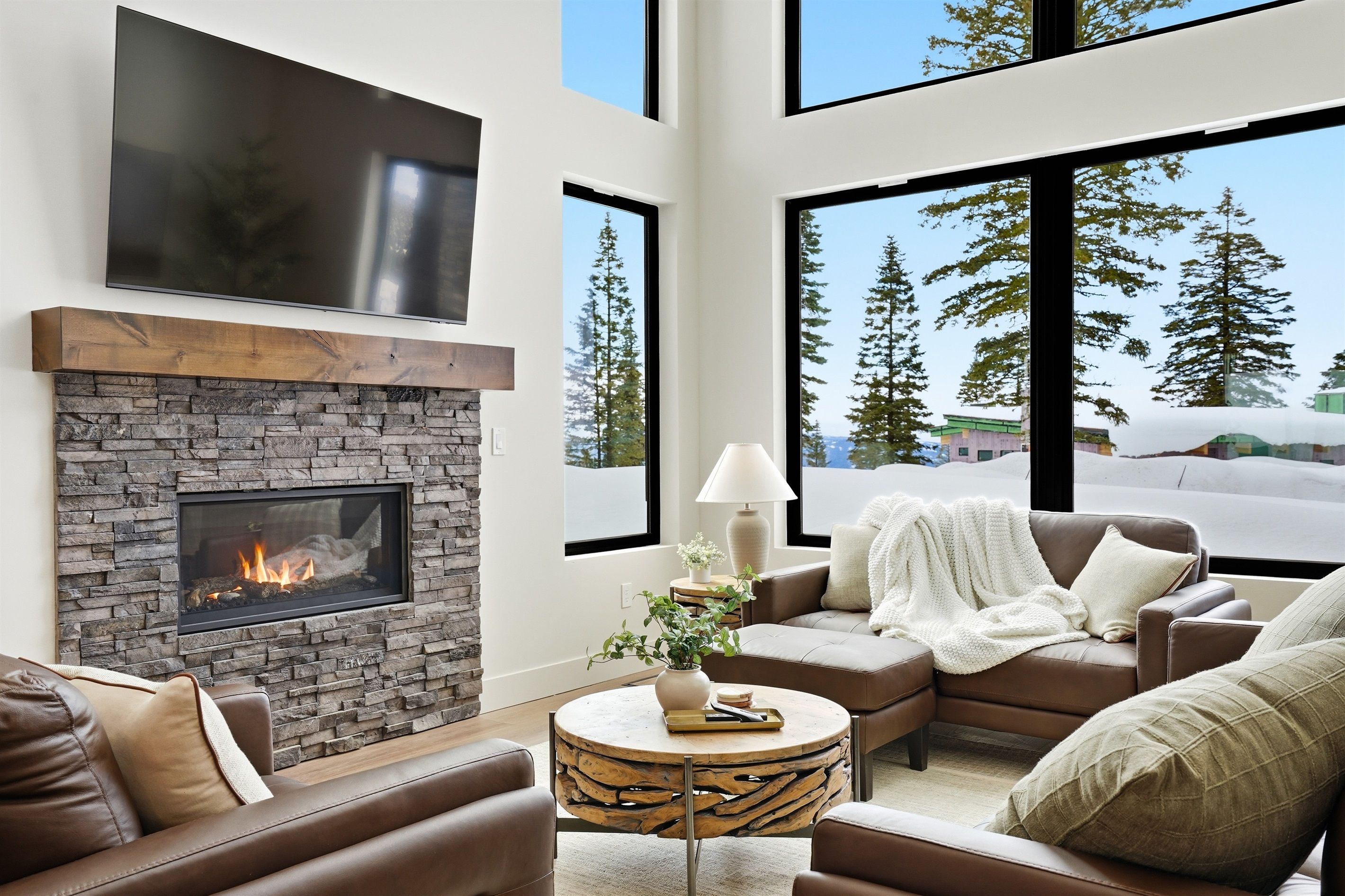 A modern living room with a stone fireplace, leather sofas, a round coffee table, and a large window offering a view of trees.