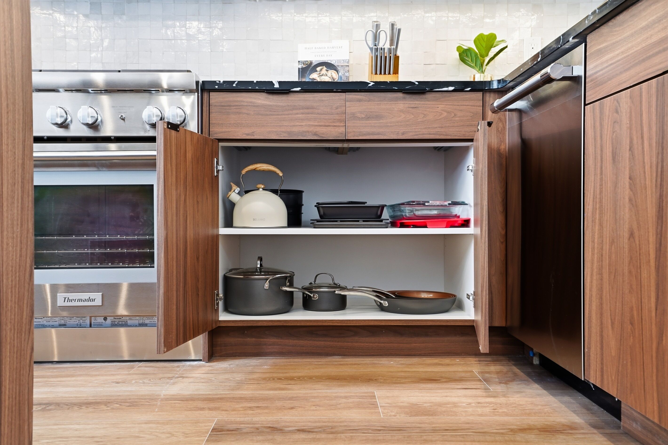 A kitchen with a Thermador oven, wooden cabinets, and a shelf with cookware.