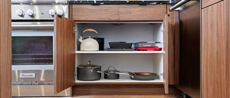 A kitchen with a Thermador oven, wooden cabinets, and a shelf with cookware.