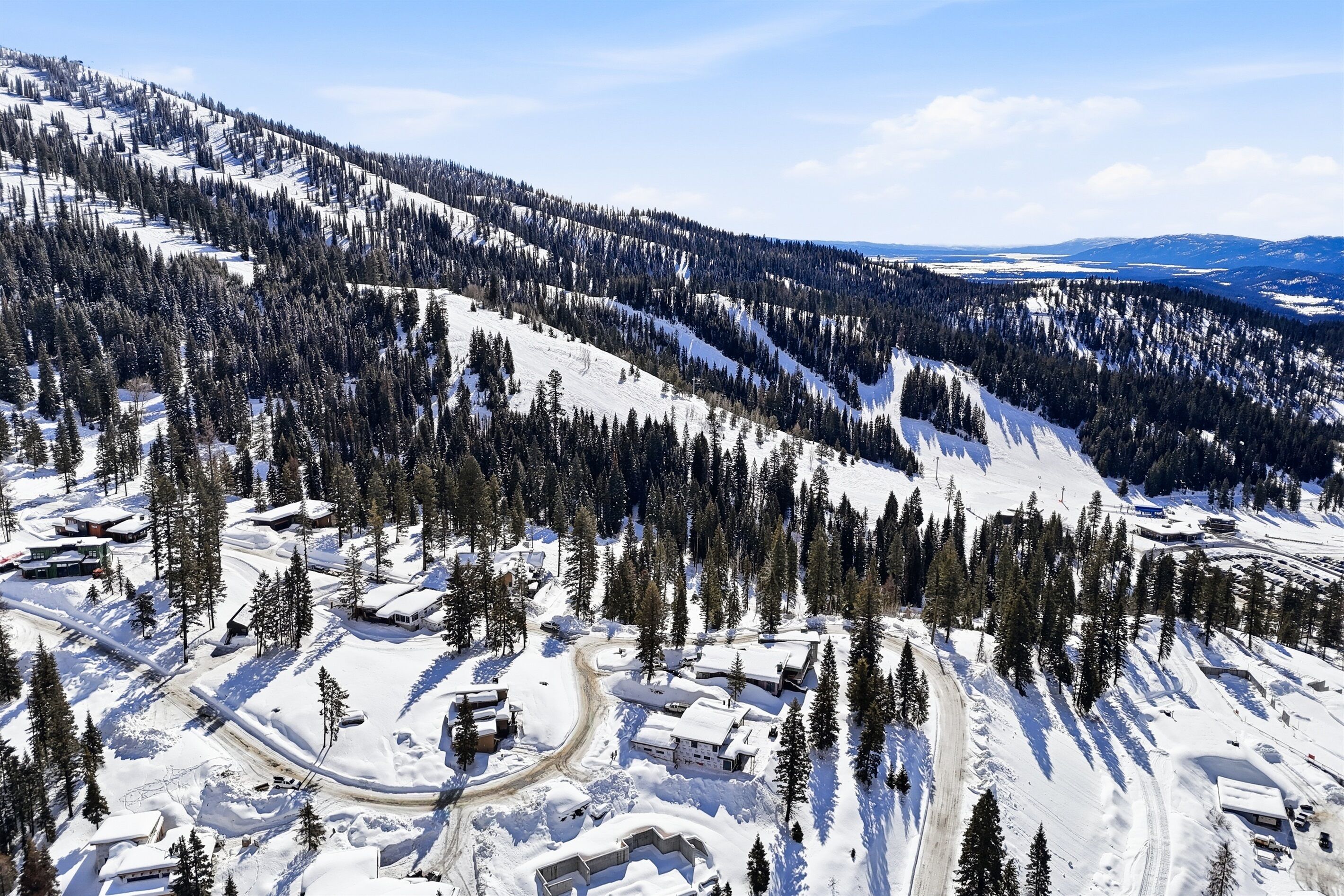 Un paisaje montañoso cubierto de nieve con una estación de esquí, que incluye pistas, alojamientos y un cielo despejado.