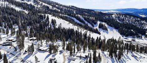 Un paisaje montañoso cubierto de nieve con una estación de esquí, que incluye pistas, alojamientos y un cielo despejado.