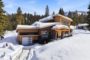 A modern two-story house with a garage, surrounded by snow-covered trees and a clear sky.