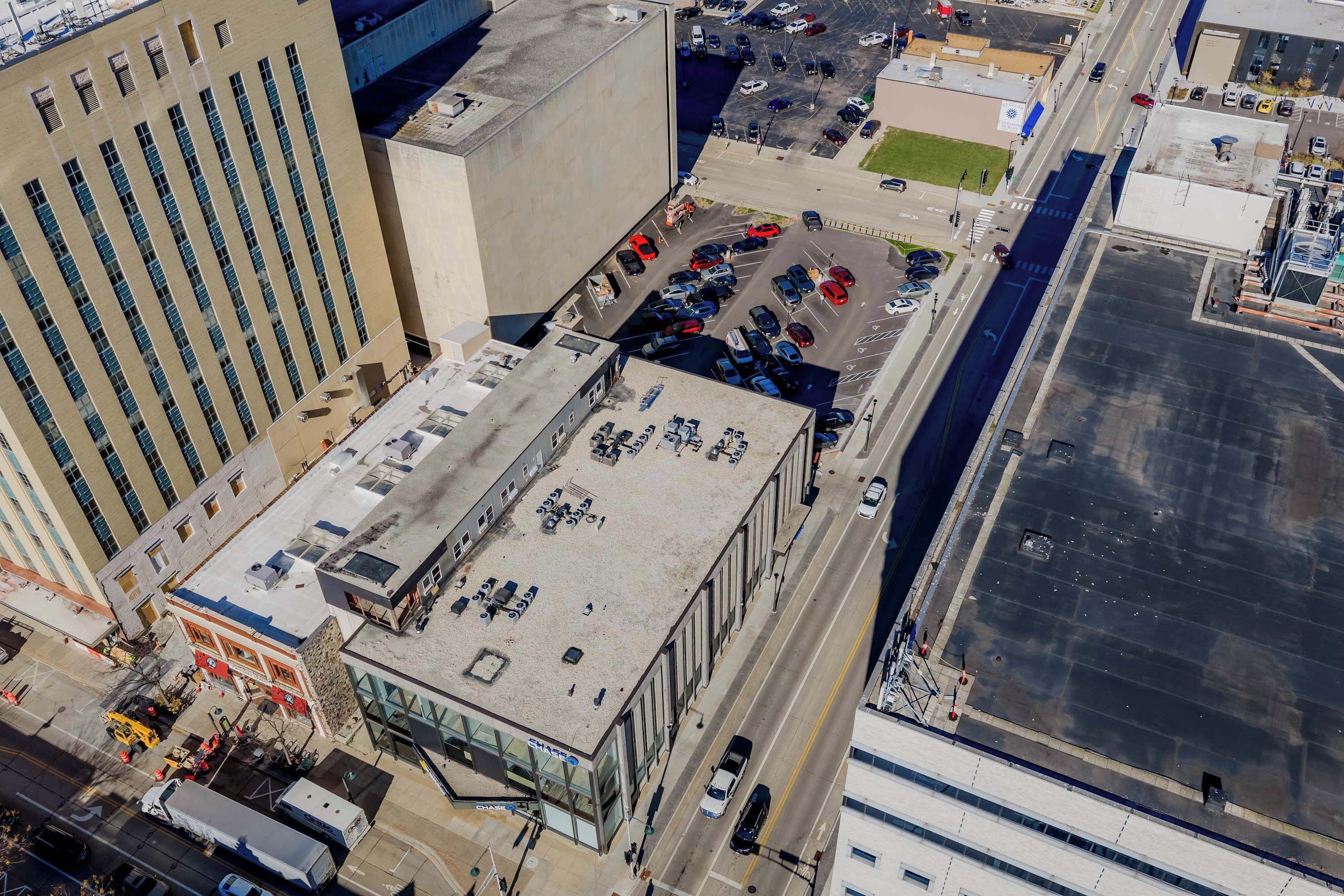 An aerial view of a building with a flat roof, multiple parking spaces, and a large open area.