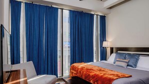 Une chambre d’hôtel avec un grand lit, un bureau et une chaise. Il y a une fenêtre avec des rideaux bleus et une vue sur la ville.