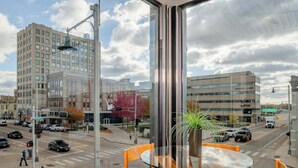 Une chambre d’hôtel moderne dotée d’une grande fenêtre donnant sur une rue animée et des immeubles.