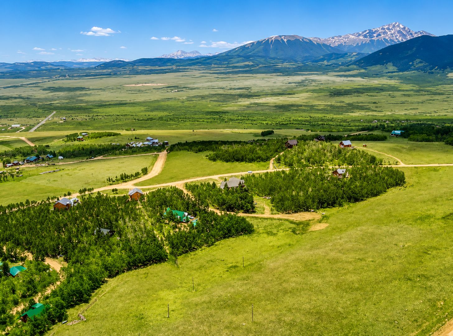 A rural landscape with scattered houses, a dirt road, and a mountain range in the background.