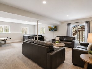 A modern living room with a sectional sofa, a coffee table, a TV mounted on the wall, and a staircase leading to an outdoor area. - Spacious Chalet W Indoor Hot Tub, Views & Private Suite (Jefferson)