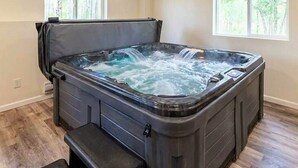 A hot tub in a room with wooden flooring and two windows.