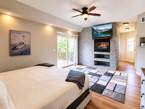 Un dormitorio con cama, chimenea, ventilador de techo y un ventanal grande.