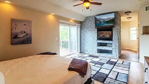 A bedroom with a bed, a ceiling fan, a stone wall, and a fireplace.