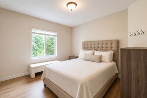 A bedroom with a large bed, a bench, a nightstand, a wardrobe, and a window with a view of greenery. - Spacious Chalet W Indoor Hot Tub, Views & Private Suite (Jefferson)
