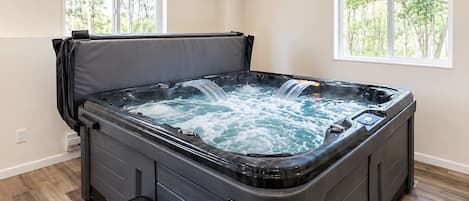 Un jacuzzi con banca, dos ventanas y vista a árboles.
