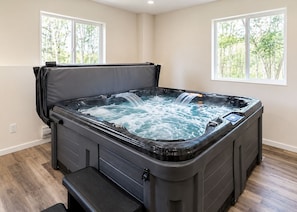 Un jacuzzi con banca, dos ventanas y vista a árboles.