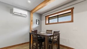 Ein Essbereich mit Holztisch und -stühlen, einer Klimaanlage, einem Fenster mit Holzrahmen und einem Bild an der Wand.