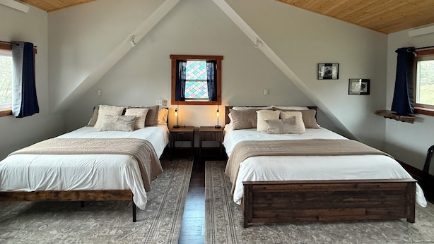 Ein Schlafzimmer mit zwei Betten, Holzboden, einem Fenster mit Buntglas und einem kleinen Regal.