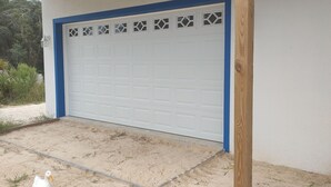 Un garage avec une porte bleue et des vitraux décoratifs, un poteau en bois et une allée en béton.