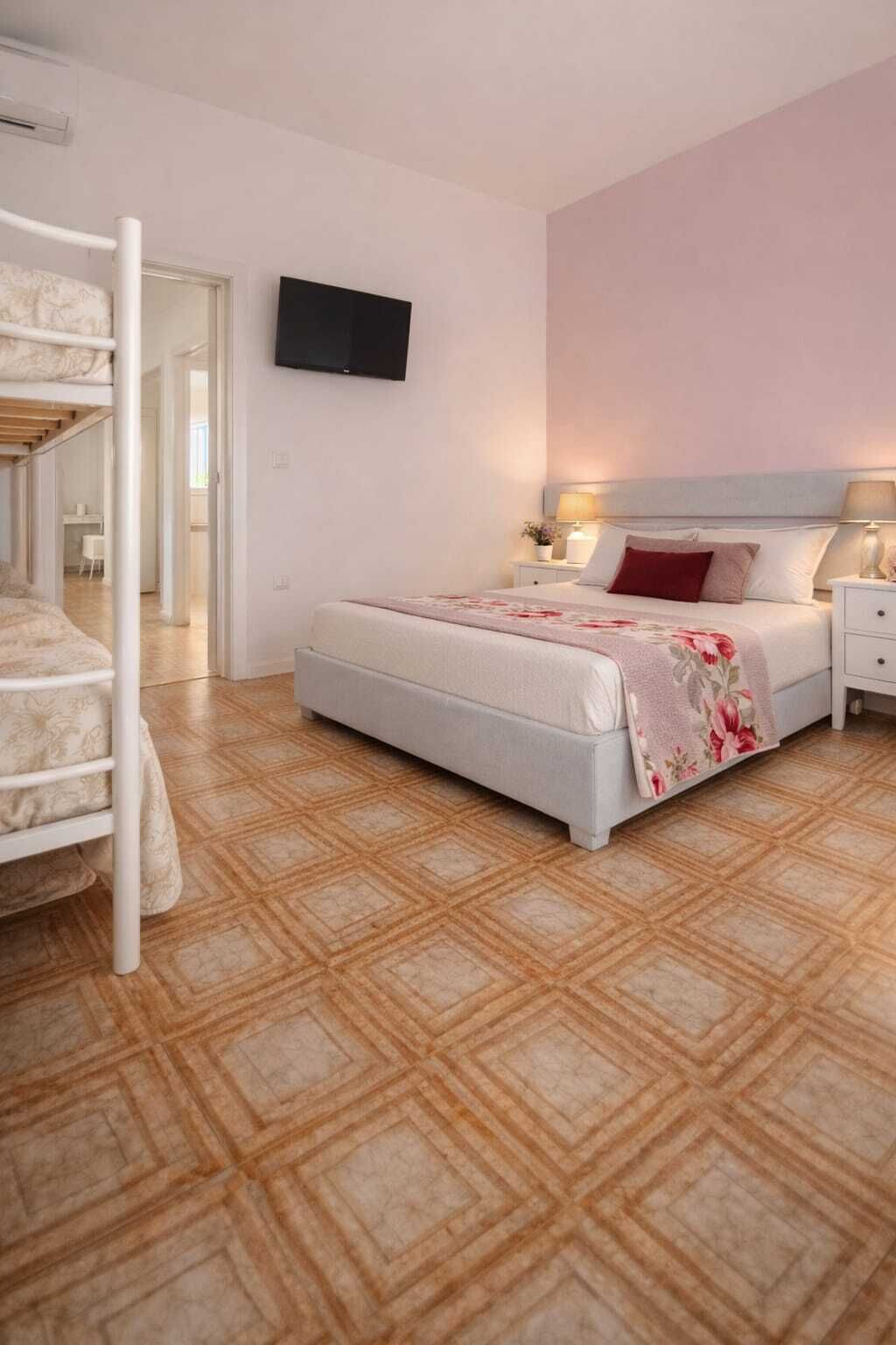 Un dormitorio con una cama litera, un televisor de pantalla plana montado en la pared, una mesita de noche con lámpara y una colcha estampada.