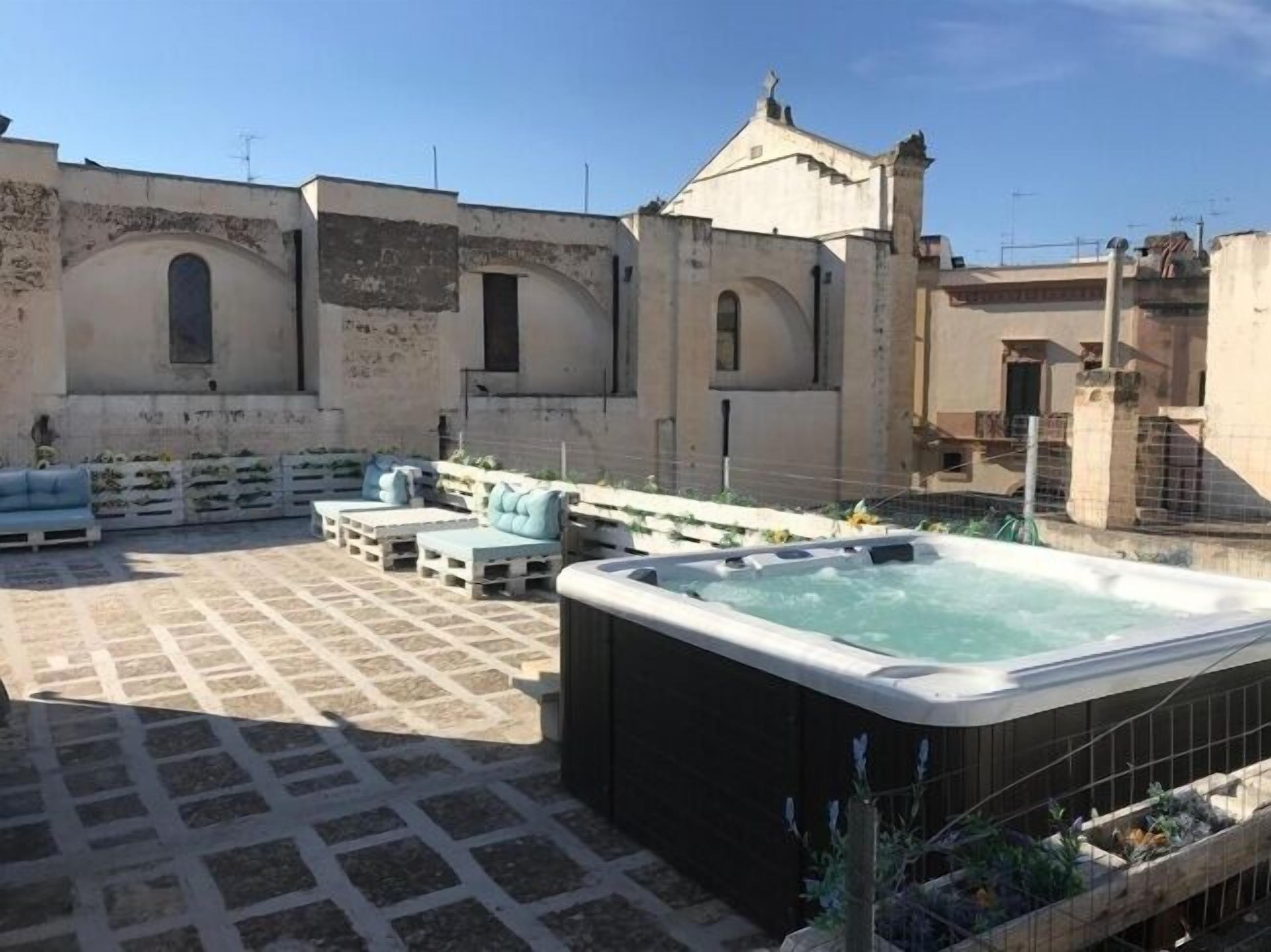 Une terrasse sur le toit avec un jacuzzi, des sièges extérieurs et un bâtiment doté de fenêtres en arc de cercle.