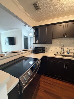 A modern kitchen with a black stove, stainless steel sink, and dark cabinets. - Terrific 2-bedroom townhome with AC in vibrant Miami (Miami)