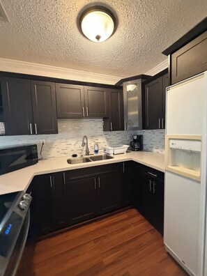A modern kitchen with dark cabinets, a white countertop, a stainless steel sink, and a white refrigerator. - Terrific 2-bedroom townhome with AC in vibrant Miami (Miami)