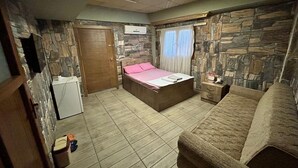 Un dormitorio con una cama, un armario de madera, una mesita de noche pequeña y una pared de piedra.