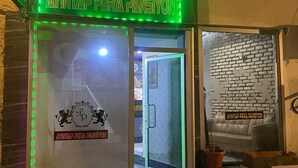 Un escaparate con un letrero de neón verde, puerta de vidrio y pared de ladrillo.