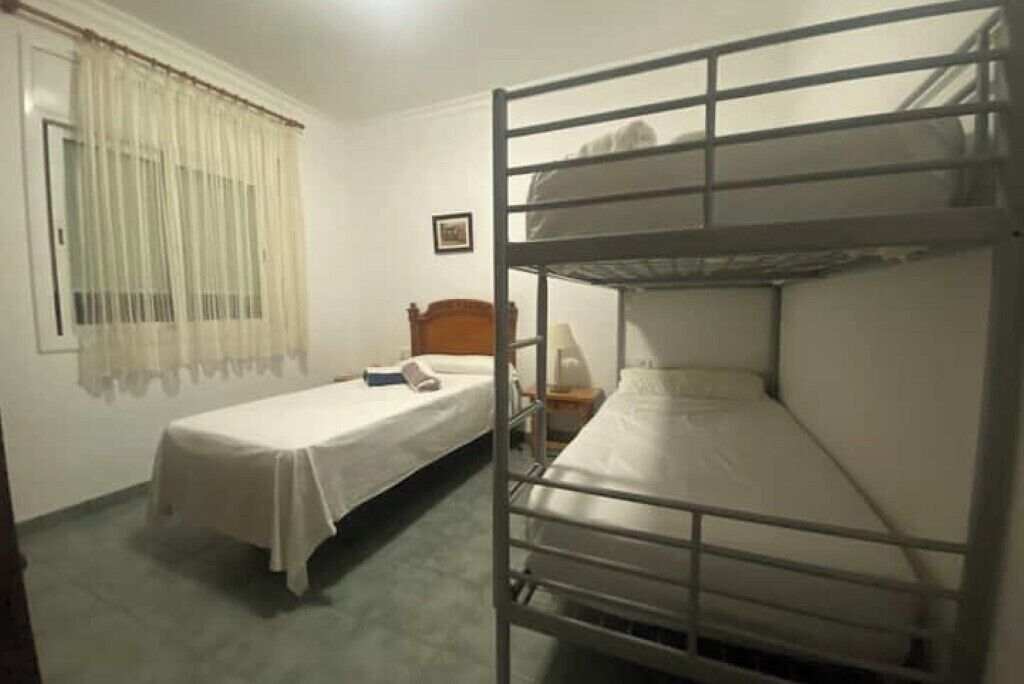 A room with bunk beds, a single bed, a bedside table, a lamp, and a window with curtains.