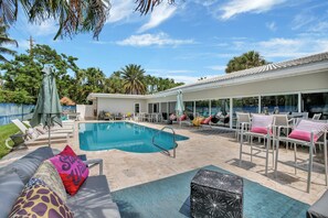 A poolside area with lounge chairs, a covered patio, and a swimming pool. - Beachfront Bliss: 6 Bedroom Home with Heated Pool (Fort Lauderdale)
