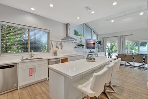 A modern kitchen with a large island, white cabinetry, and a view of the outdoors. - Beachfront Bliss: 6 Bedroom Home with Heated Pool (Fort Lauderdale)