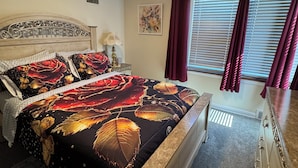 Un dormitorio con cama, cómoda, mesita de noche, lámpara, ventana con cortinas y una obra de arte colgada en la pared.