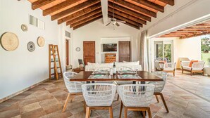 A spacious dining area with a wooden ceiling, white wicker chairs, and a central table set for dining. - Las Quintas 6B - 2BR Chic Condo on Golf Course/SDC Hotel Zone, Beach & Dining. (San José del Cabo)