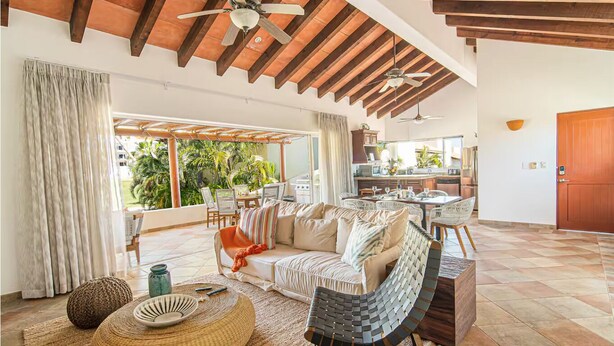 A spacious living area with a large sofa, a dining table, and a kitchen in the background. - Las Quintas 6B - 2BR Chic Condo on Golf Course/SDC Hotel Zone, Beach & Dining. (San José del Cabo)