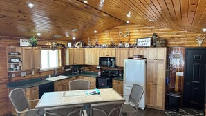 Una cocina acogedora de estilo cabaña, con armarios de madera, una mesa de comedor con sillas, un refrigerador y un lavamanos.