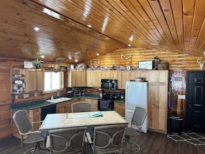 L’intérieur d’un chalet en bois chaleureux, avec une cuisine, un coin repas et une porte noire.