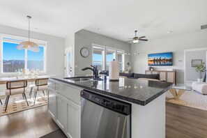 A modern kitchen with a large island, stainless steel appliances, and a dining area with bar stools. - Haven in the Desert - Kennewick spacious home (Kennewick)