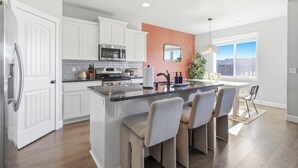 A modern kitchen with white cabinets, a central island with bar stools, a large window with a view, and a hanging light fixture. - Haven in the Desert - Kennewick spacious home (Kennewick)