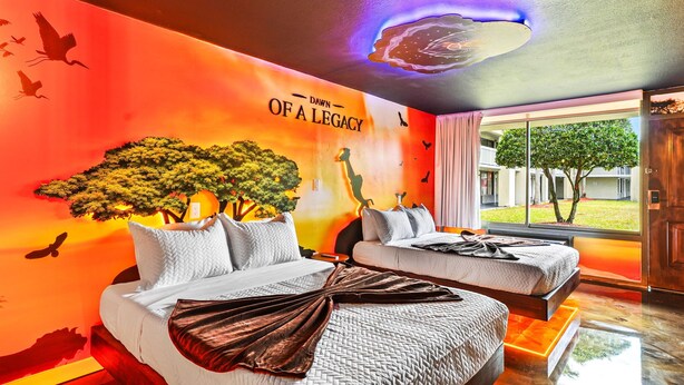 A hotel room with two beds, a mural of a tree and a giraffe, and a view of the outdoors. - Lion King studio w/ pool & workspace (Kissimmee)