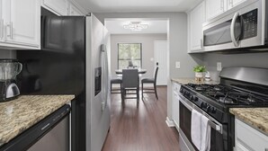 A modern kitchen with white cabinets, a black refrigerator, a microwave, a stove, and a granite countertop. - Premium Townhome #A w/ 2 King Beds & Luxury Baths (Peachtree Corners)